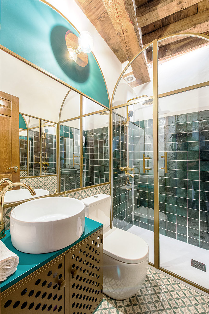 Baño de estilo art deco con azulejos verdes en acabado brillo y mampara dorada.
