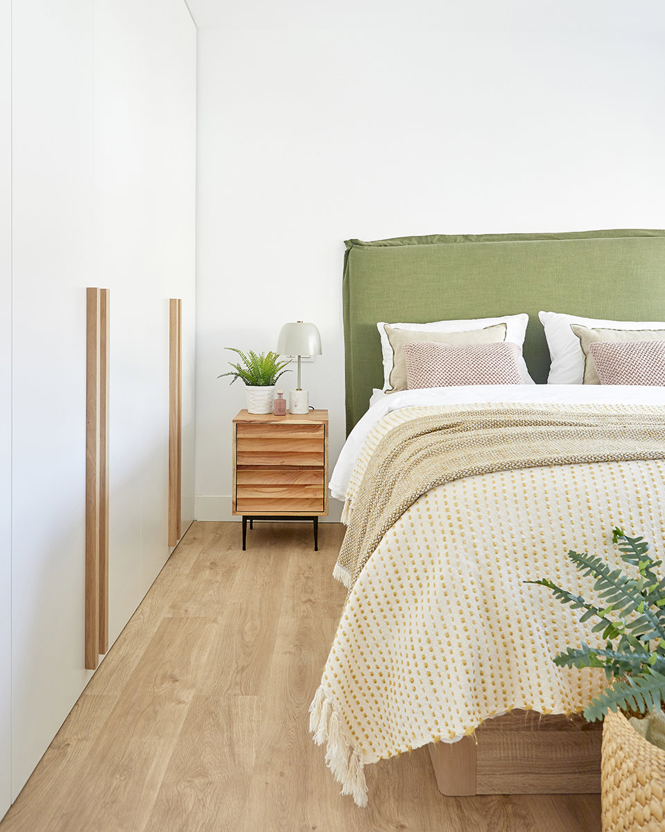 Dormitorio matrimonio con mesita de madera y cabecero tapizado verde.