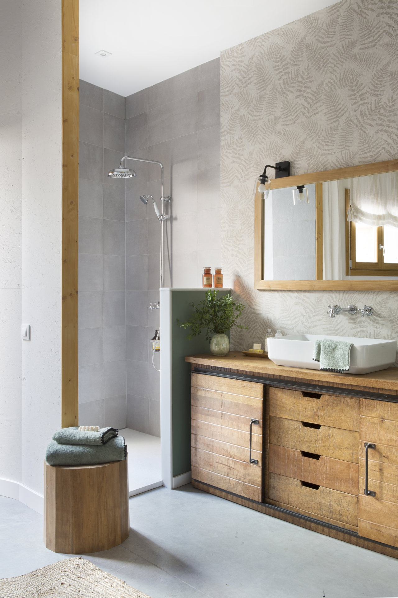 Baño pequeño y abierto al dormitorio con un pequeño murete como alternativa a la mampara dela ducha. Es un diseño de la interiorista Pia Capdevila. 