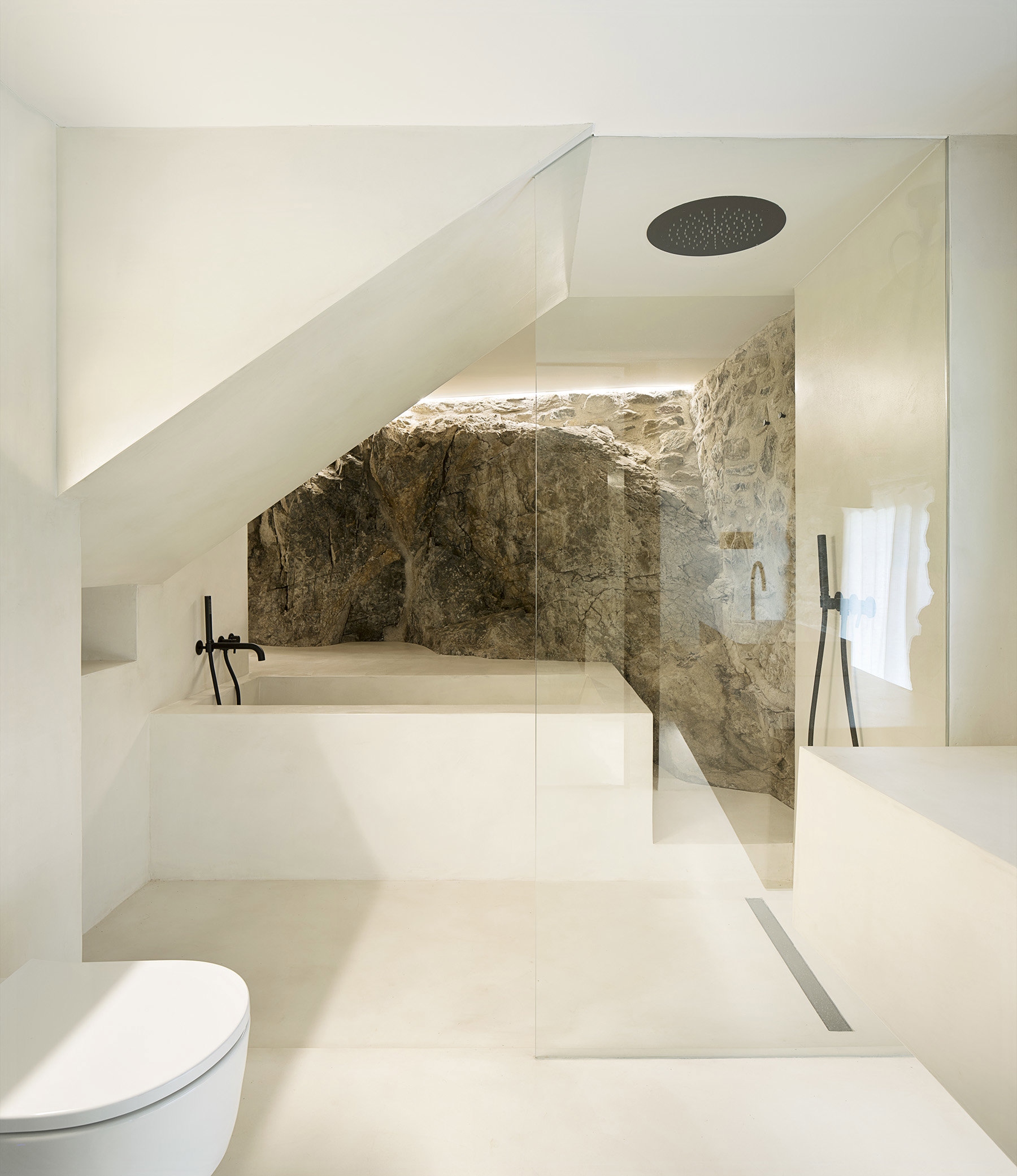 Baño blanco con pared de piedra y mampara transparente