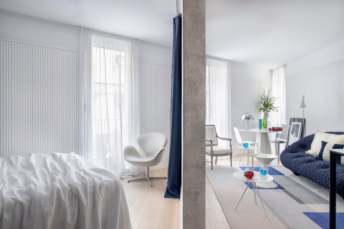 Salón minimalista y blanco con columna de hormigón y sofá azul