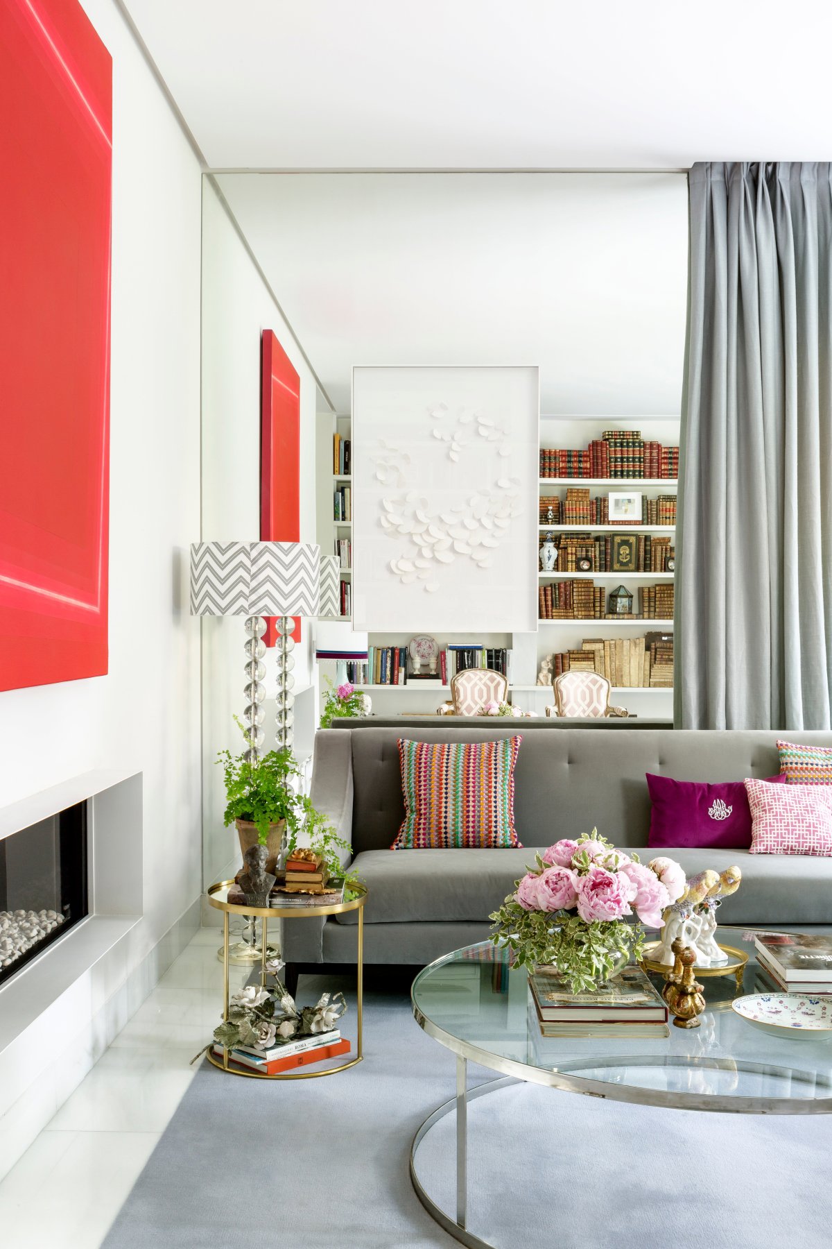 Salón pequeño con espejo en la pared, sofá gris y gran cuadro rojo sobre la chimenea