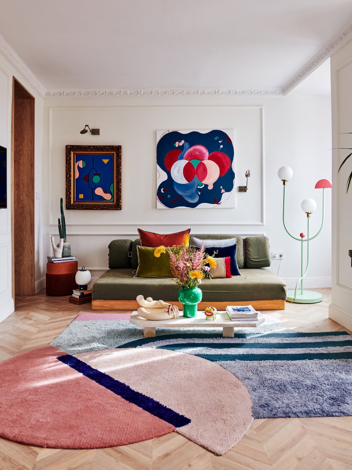 Pequeño salón formado por un sofá verde, cuadros de colores y una alfombra de original forma