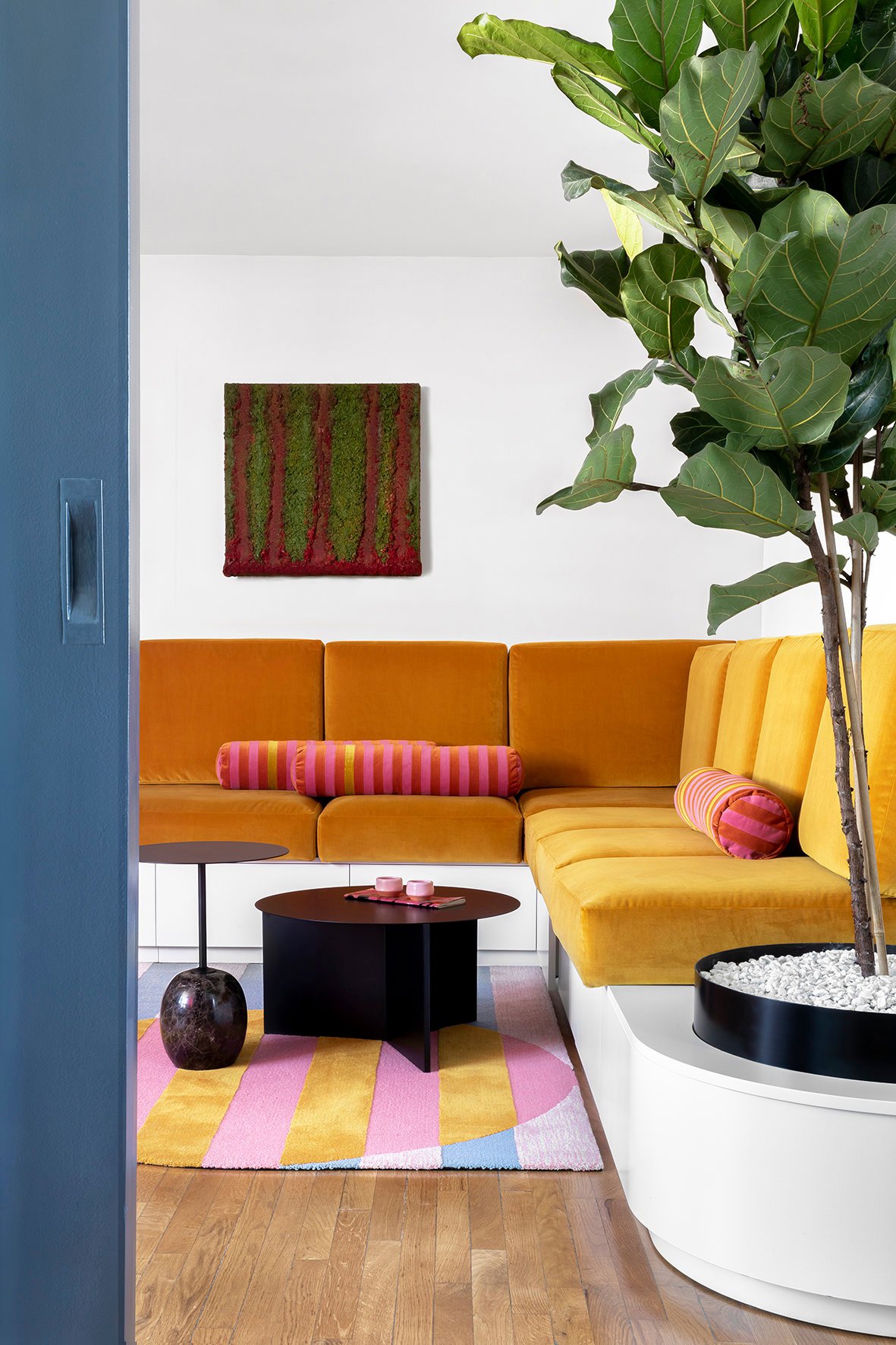 Salón pequeño con sofá mostaza, mesa en negro y textiles de colores