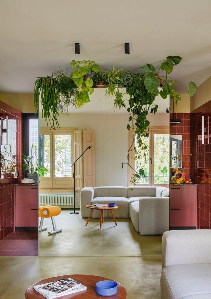 Salón pequeño con espejo, plantas, sofá blanco y cocina escondida