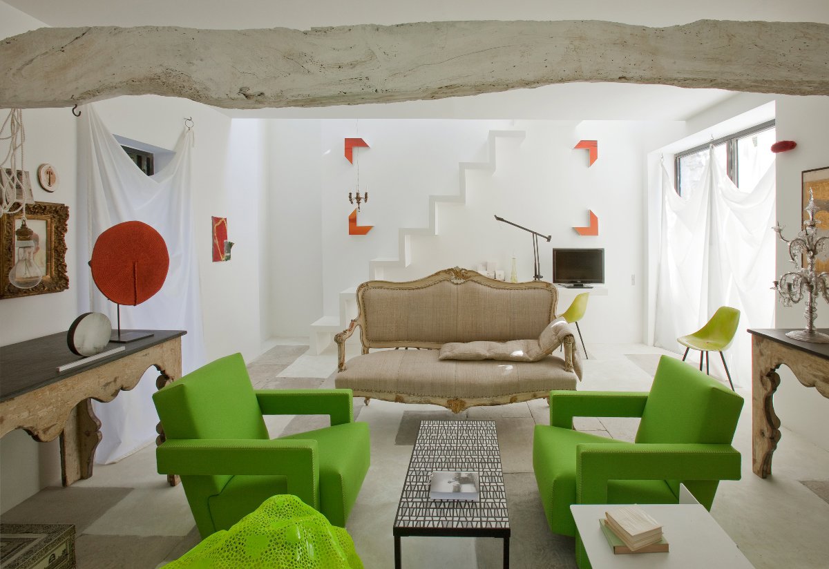Salón pequeño con sofás verdes, viga de hormigón y escaleras en blanco