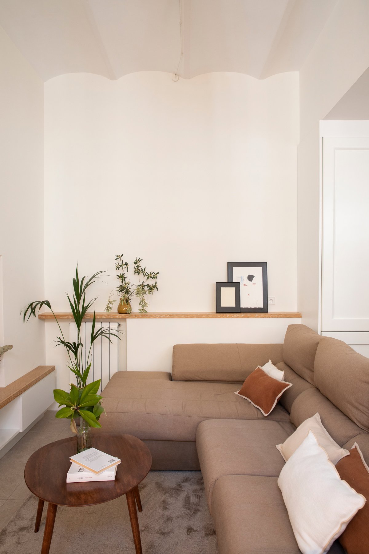 Salón pequeño con sofá marrón esquinero, repisa de madera y plantas