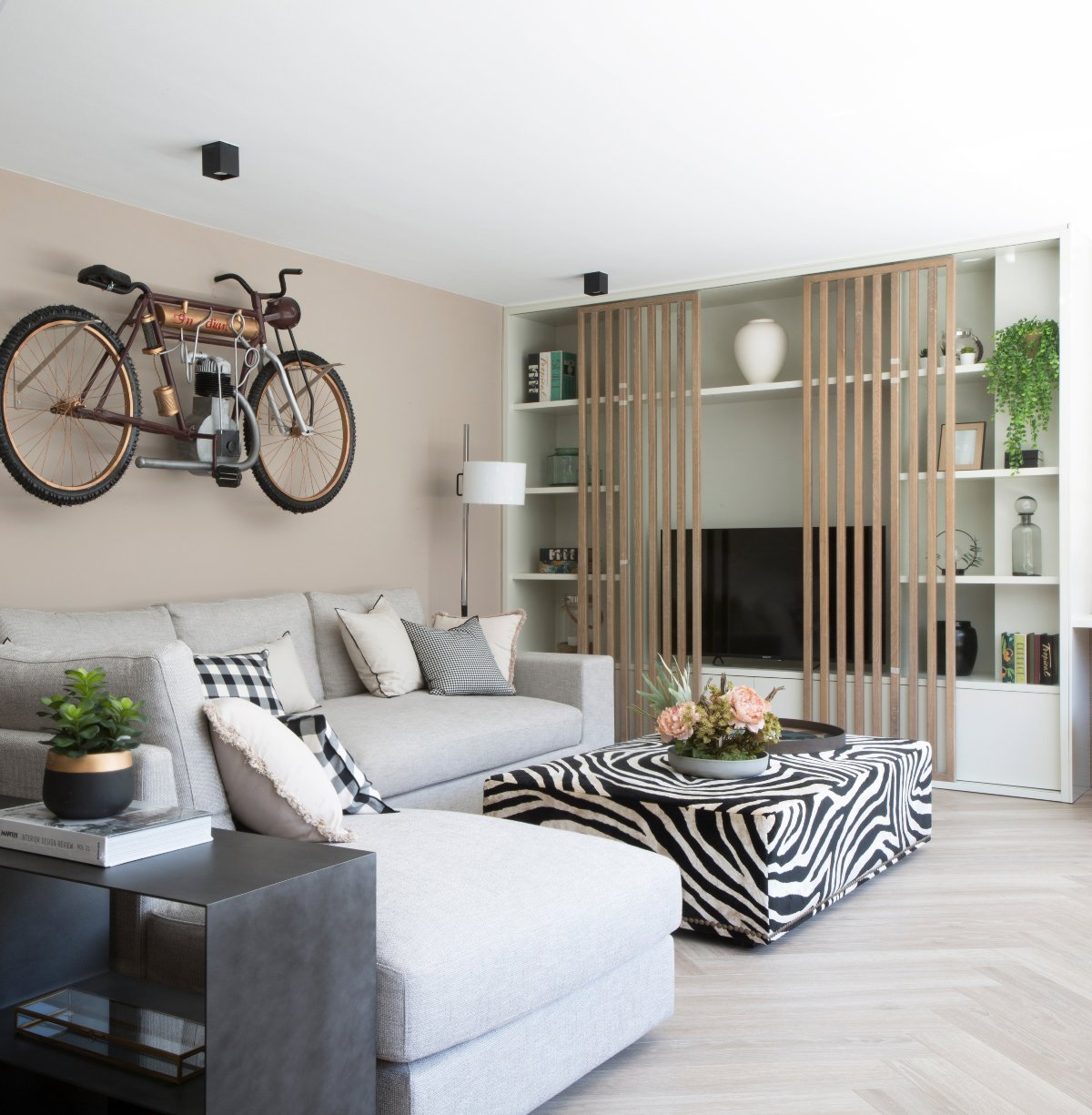 Salón pequeño con escultura de bicicleta, sofá gris y mesilla de cebra