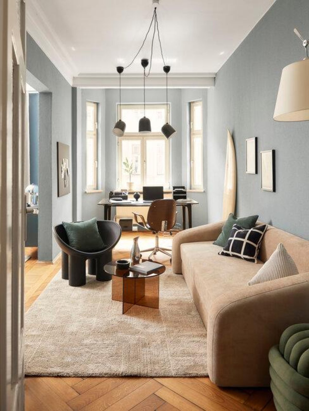 Salón pequeño con  pared azul grisácea, escritorio bajo la ventana y sofá marrón