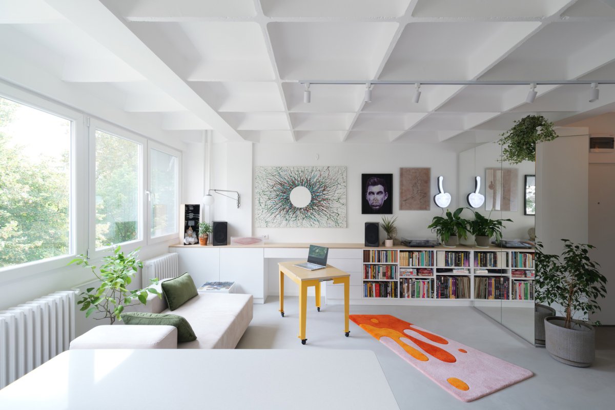 Salón pequeño con alfombra de vivos colores, biblioteca baja y sofá blanco