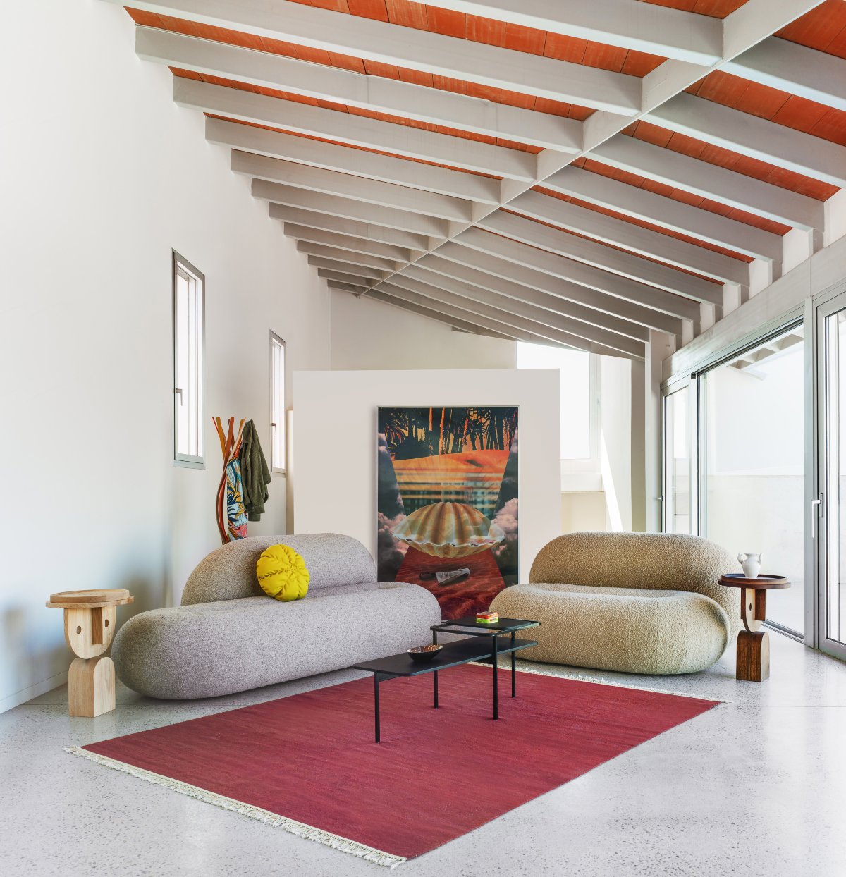 Salón pequeño con alfombra roja, sofás redondos y cuadro con un motivo de concha