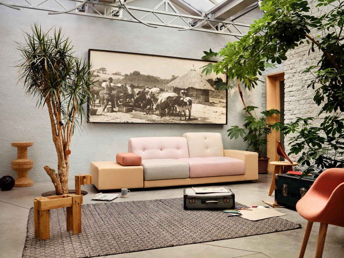 Salón pequeño con sofá rosa, maletas decorativas, plantas y cuadro con vacas