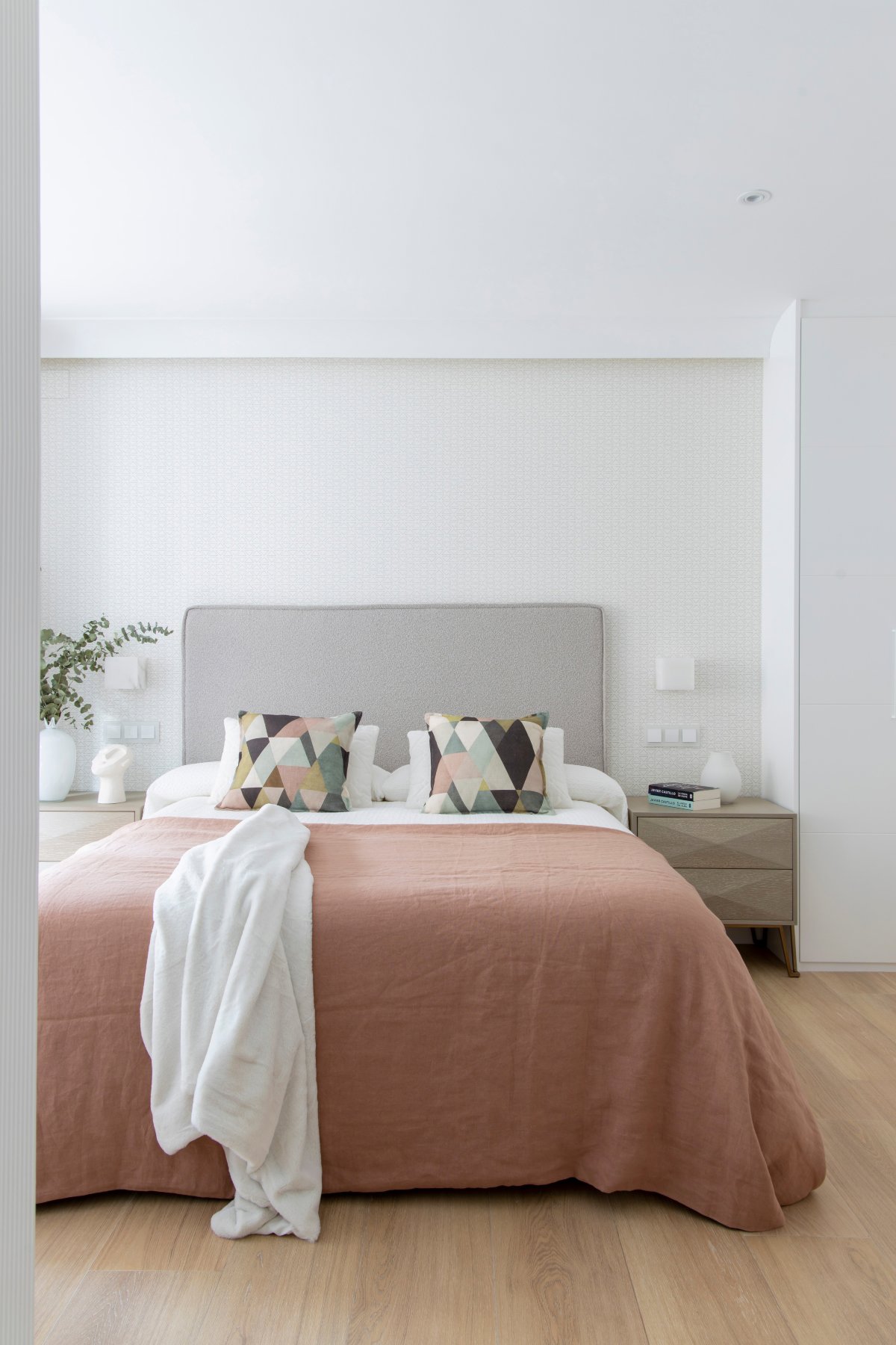 Dormitorio con papel pintado en el cabecero y colcha rosa palo