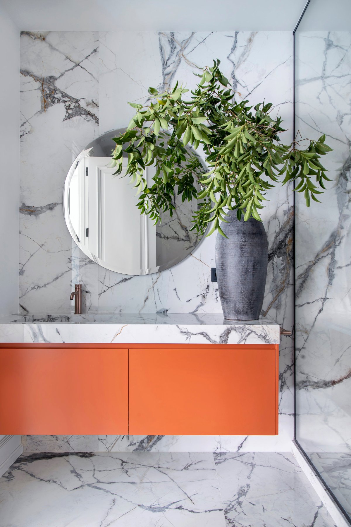 Baño moderno en mármol y muebles naranjas 