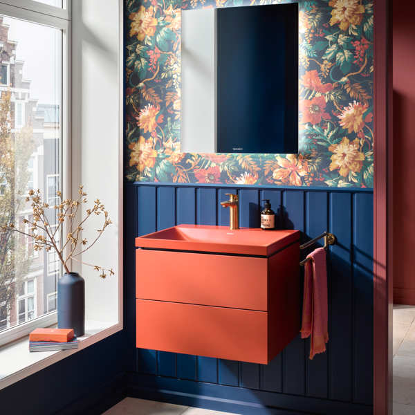 Baño con lavabo rojo, papel pintado de flores y zócalo de madera azul 