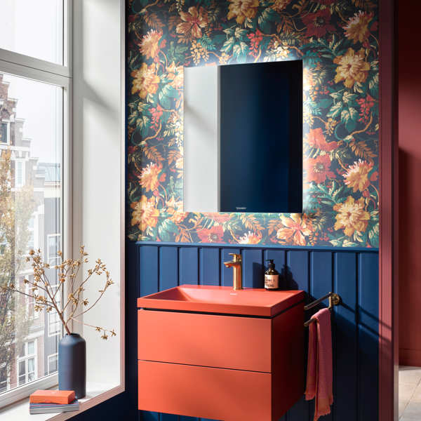 Baño con lavabo rojo, papel pintado de flores y zócalo de madera azul 