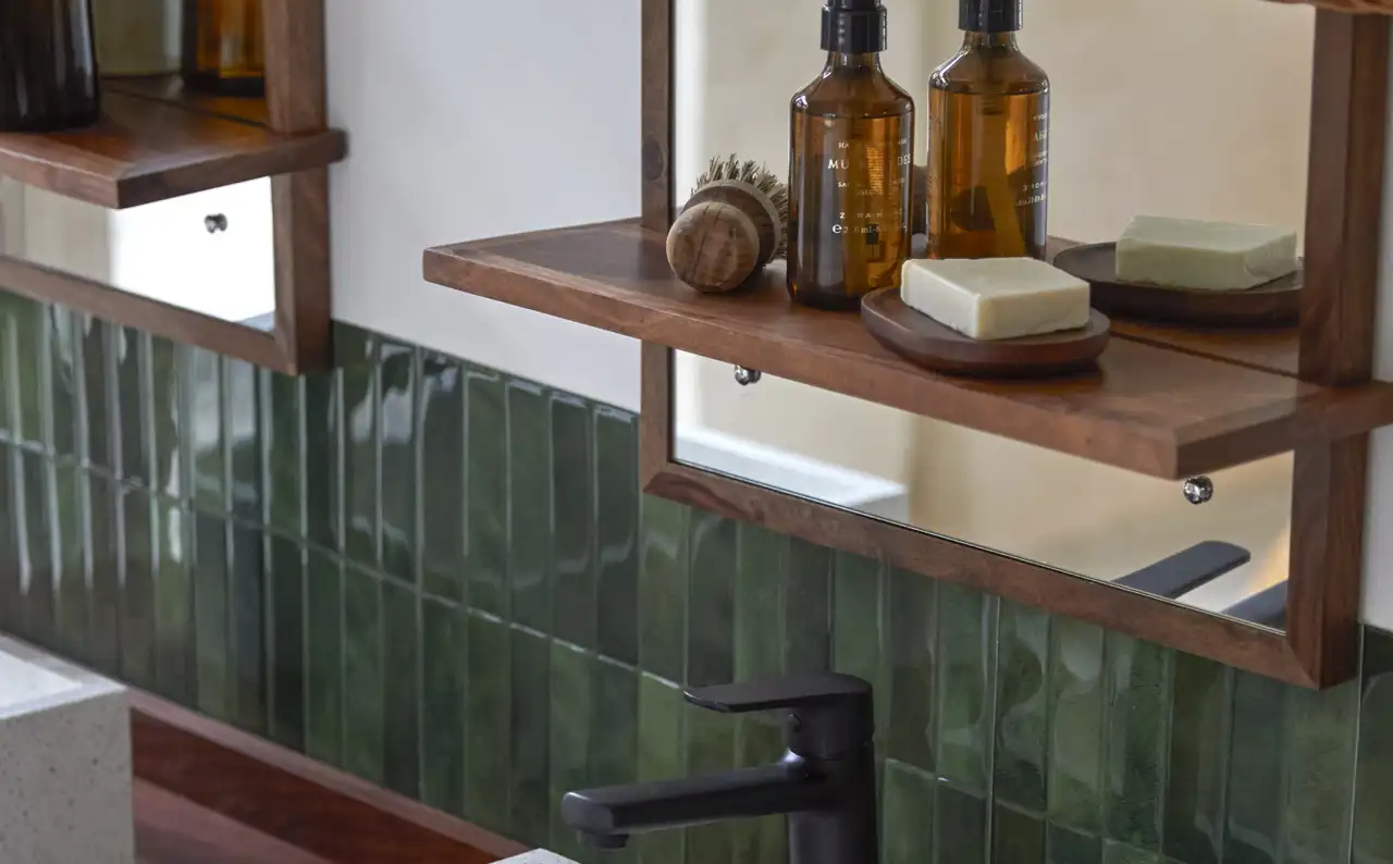 Baño con azulejos verdes, lavabo cuadrado y espejo con repisa de madera