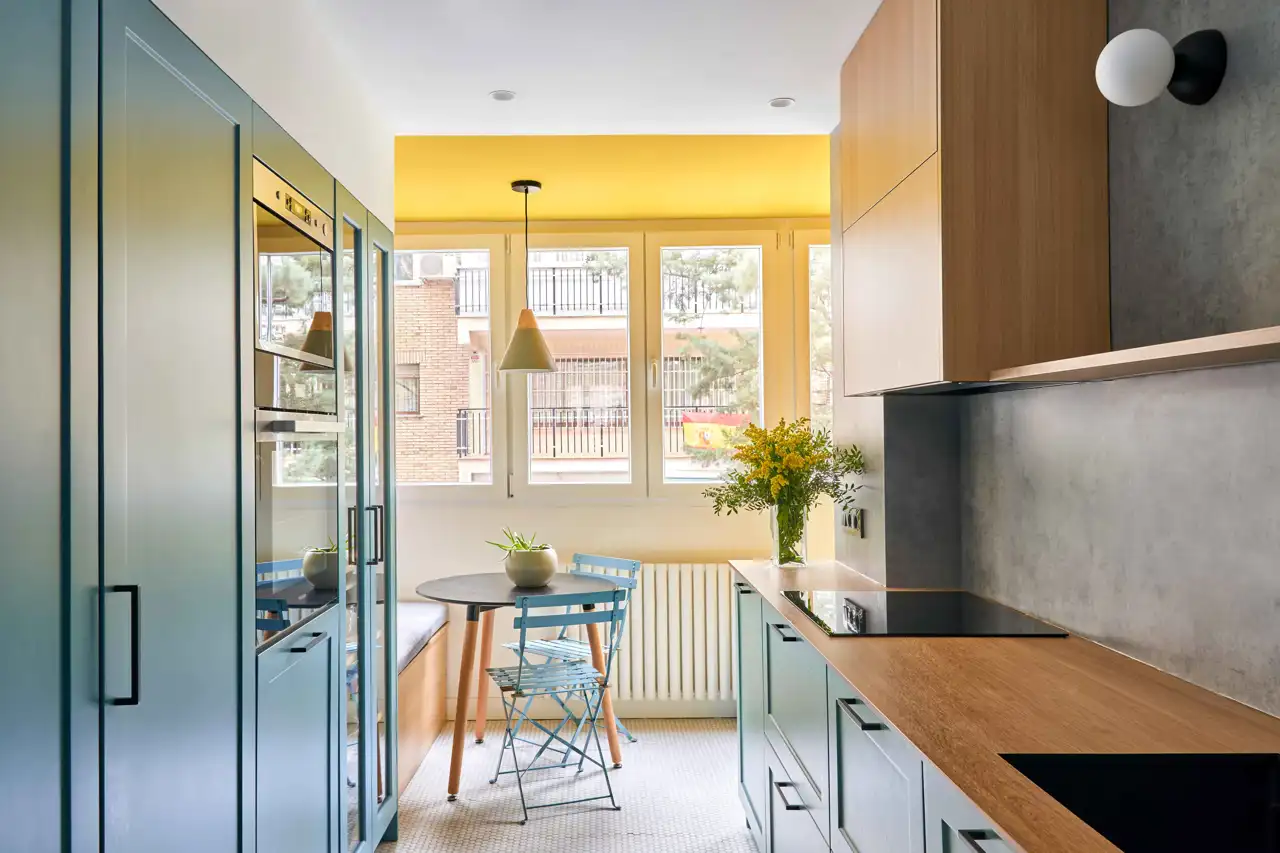 Una bonita cocina con armarios en azul grisáceo y madera. El office, con el techo en amarillo, aporta una nota diferencial