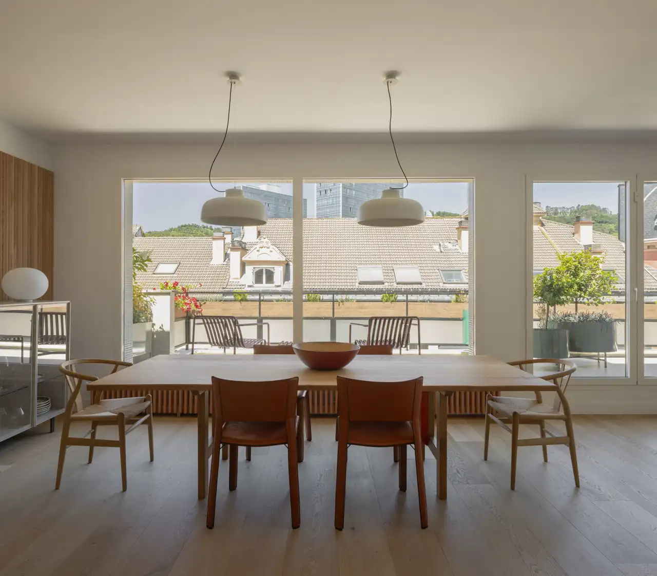 COMEDOR. La mesa es de Arkaia, la lámpara es de Santa & Cole y las seis sillas son el modelo CH4 Wishbone Chair, de Carl Hansen & Son. Al fondo, en la terraza, butacas de Hay.