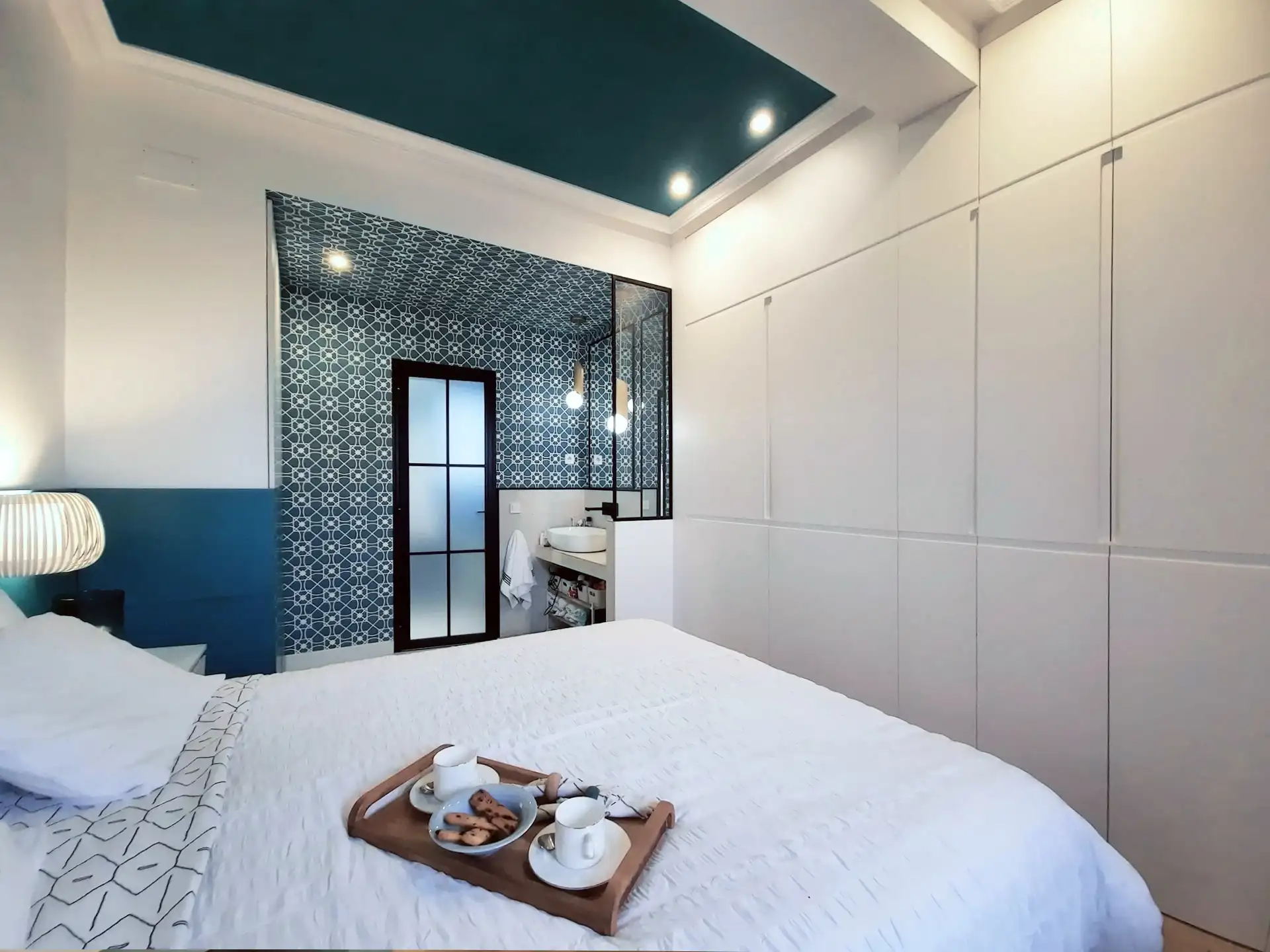 habitacion en tonos blancos y azules con grandes armarios y baño con papel imitando hidraulico tambien en techoy metal estilo eclectico