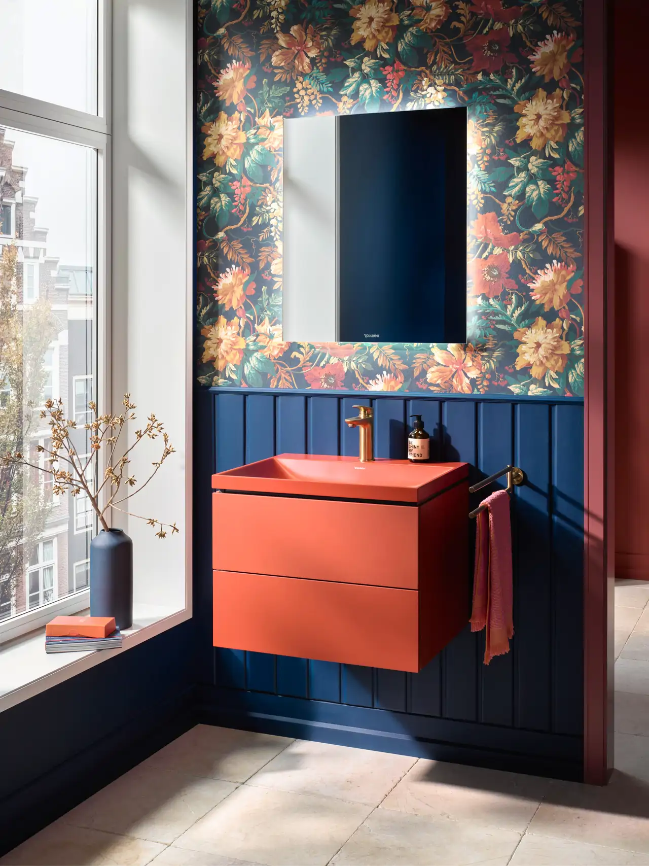 Baño con lavabo rojo, papel pintado de flores y zócalo de madera azul 