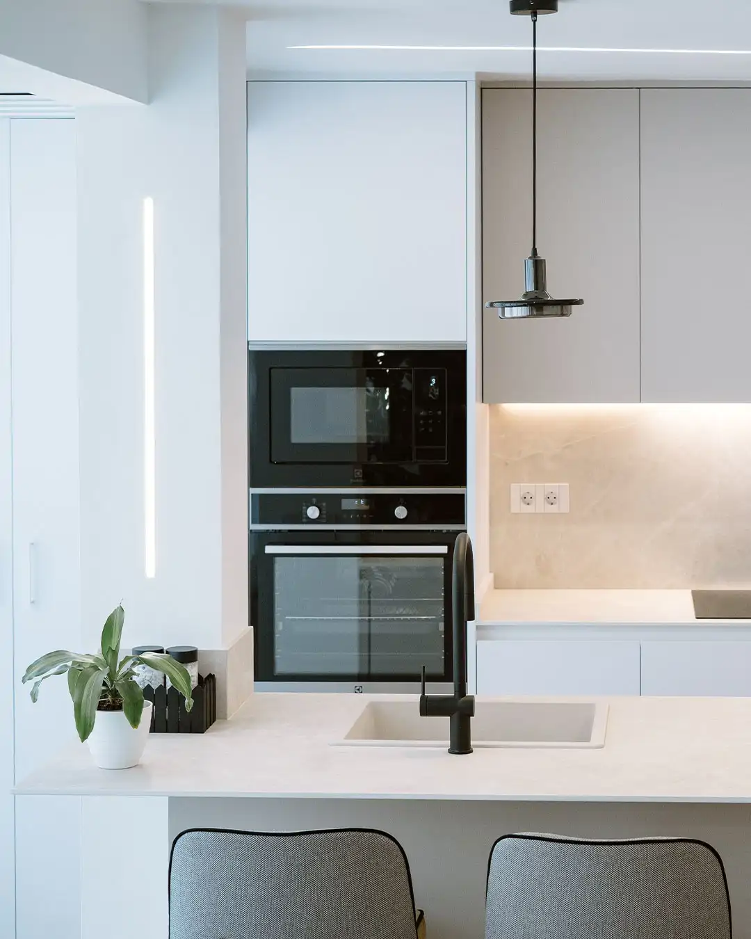 Cocina con isla en tonos blancos y torre de electrodomésticos