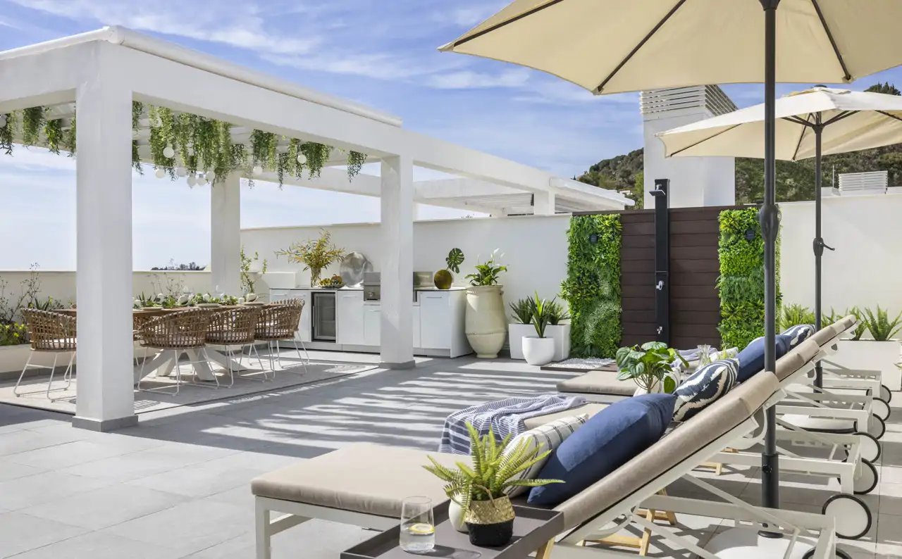 Una terraza en un ático con cocina exterior, zona de tumbonas y una ducha