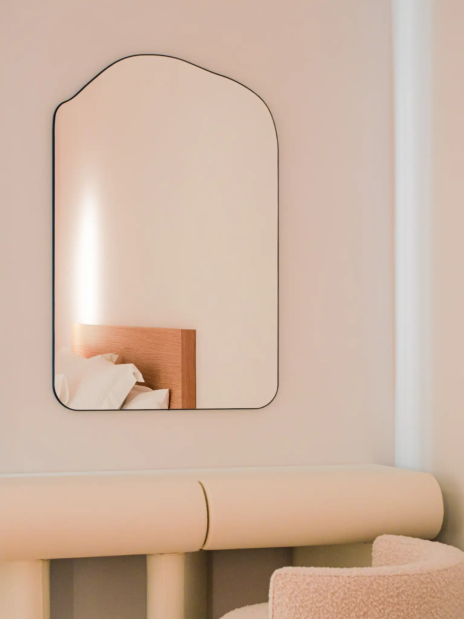 dormitorio blanco con butaca bouclé y espejo orgánico