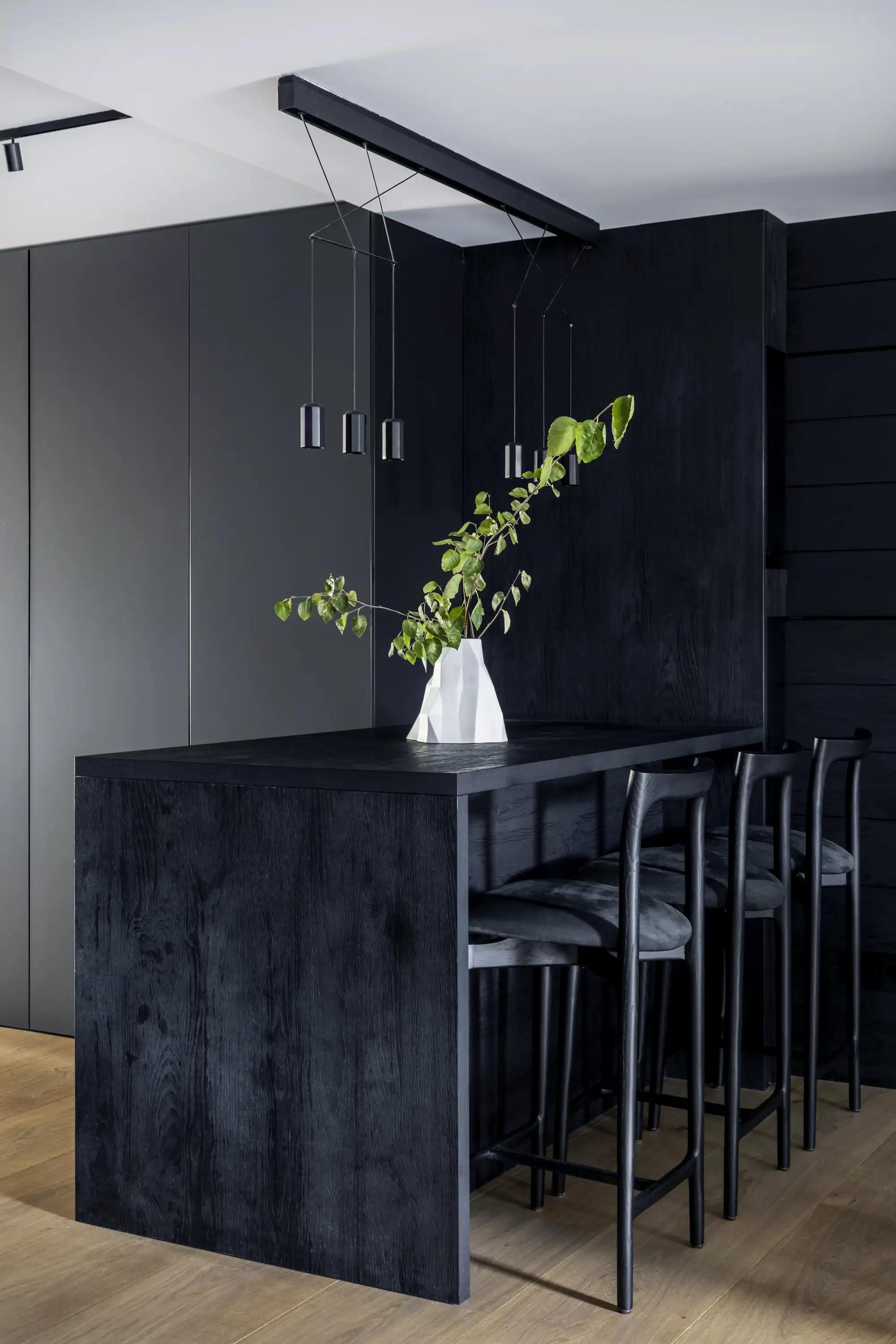 cocina negra isla con isla y taburetes también en negro y suelo de madera